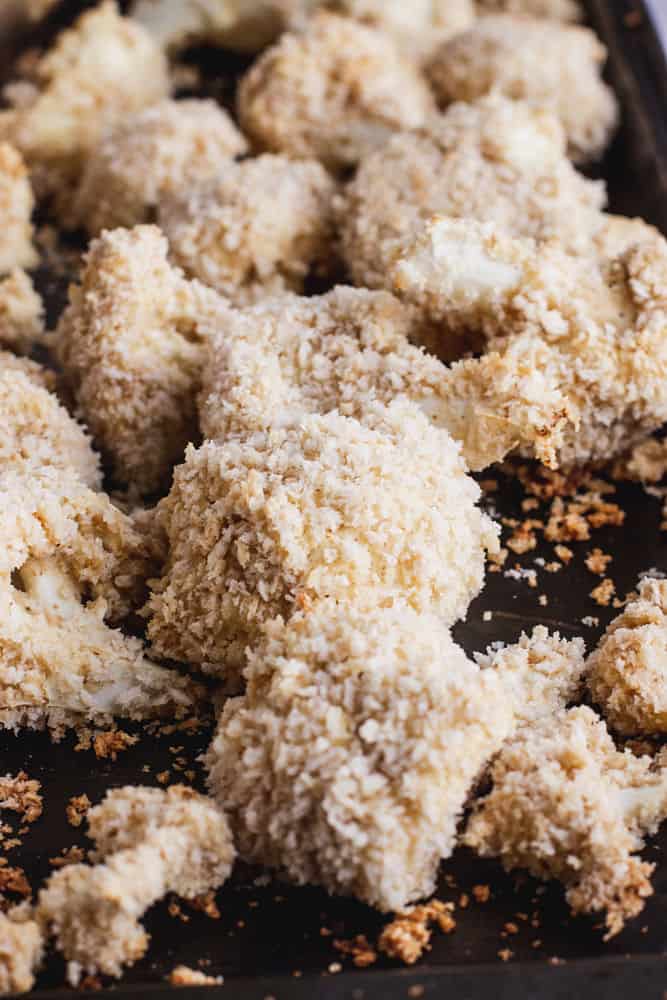 A close-up of breaded cauliflower florets on a baking sheet