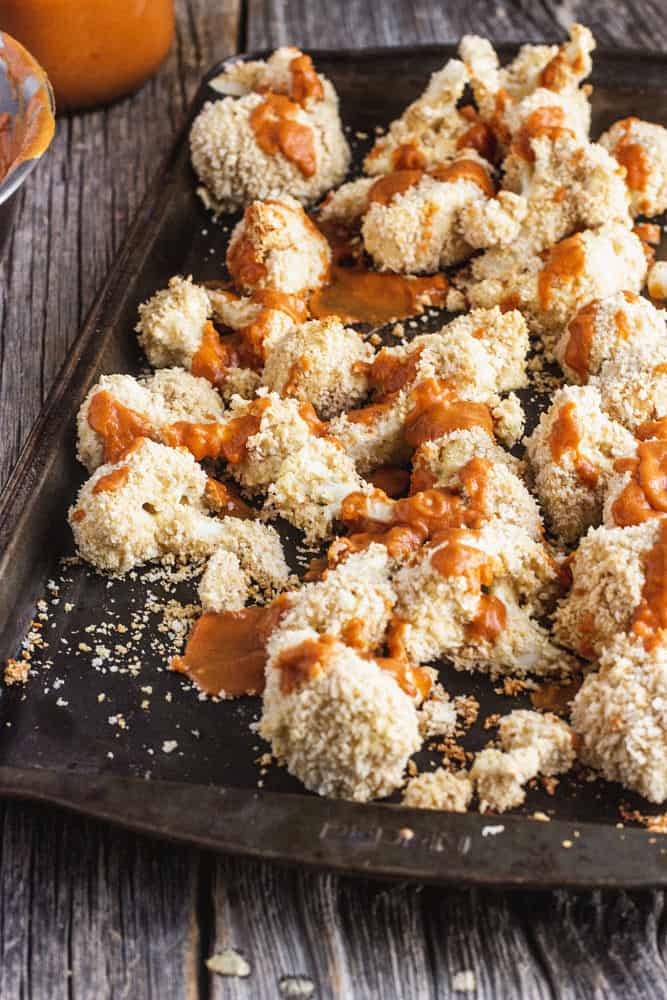 Breaded cauliflower florets being covered in hot sauce