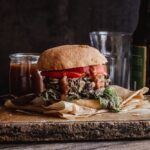 A burger on a thin wooden board with ketchup oozing our of it