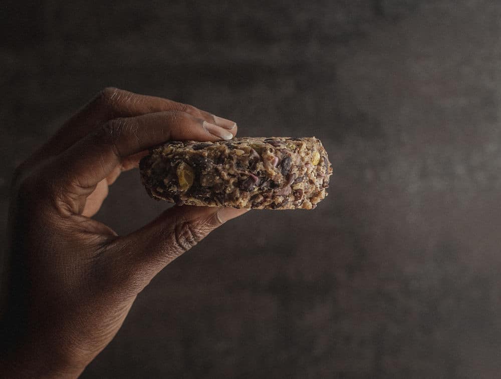 A dark-skinned hand holding a veggie patty in front of a dark background