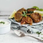 Ramekin with yogourt sauce next to fritters on a small plate with lime wedges