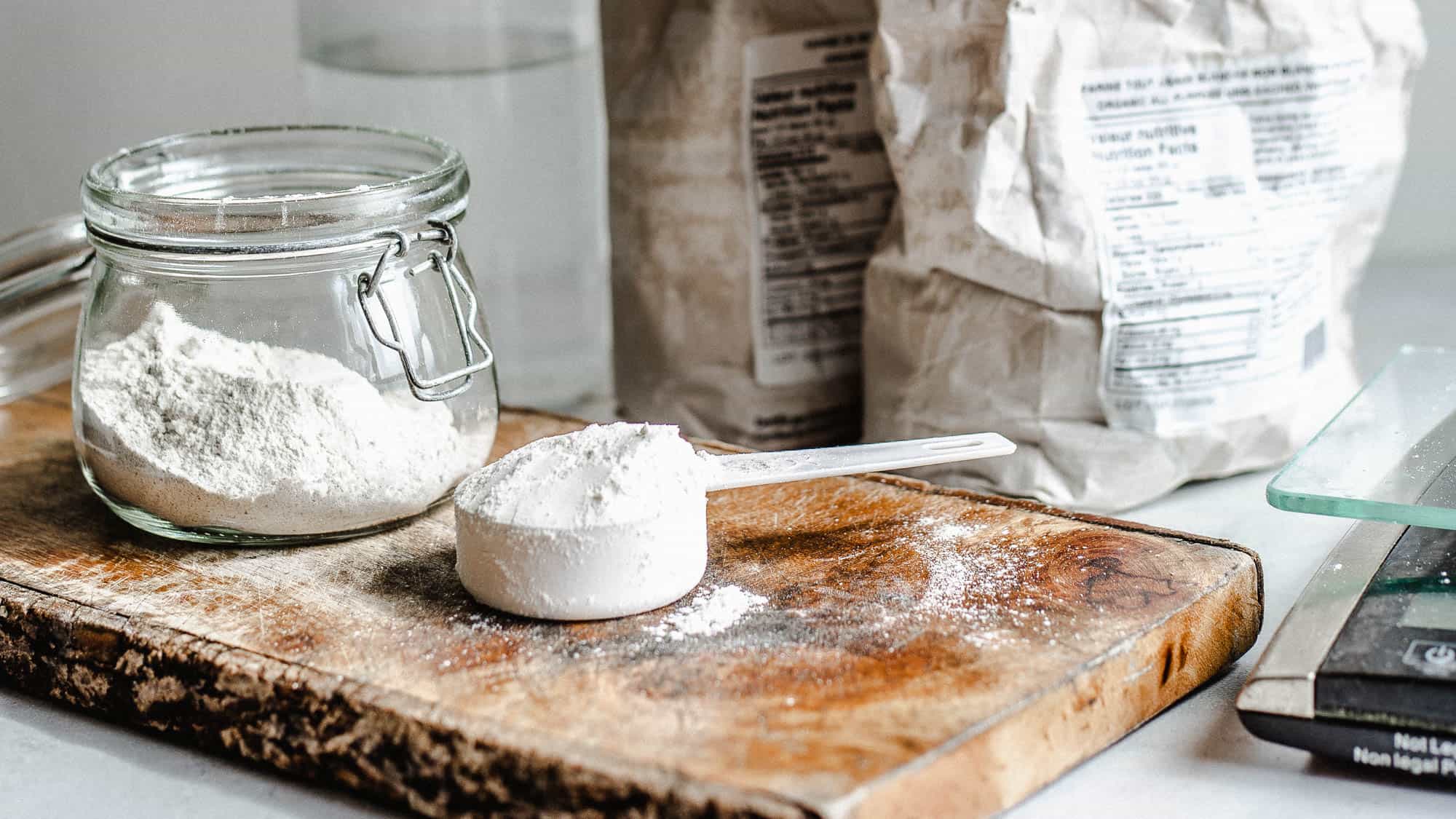 Farine blanche dans un petit pot Mason et farine blanche dans une petite tasse à mesurer blanche