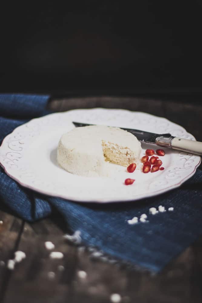 Cheese-looking round food with a on a salad plate with pomegranate arils next to it