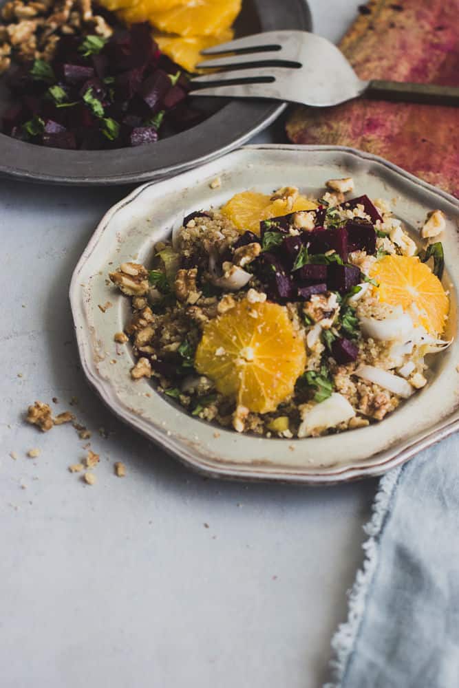 Quinoa Salad with Beets, Oranges and Walnuts in a rustic metallic plate with another plate of ingredients in a metallic plate behind