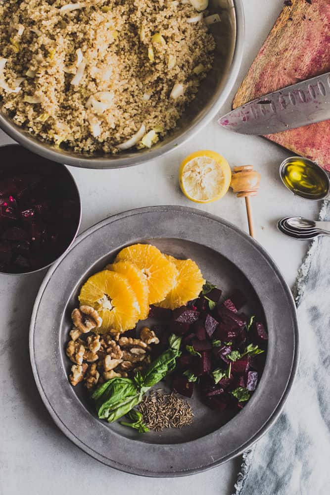 Vue de dessus de la salade de quinoa aux betteraves et aux noix. Dans le sens des aiguilles d'une montre : oranges tranchées, betteraves cuites en cubes, graines de cumin, feuilles de basilic, noix sur une plaque métallique