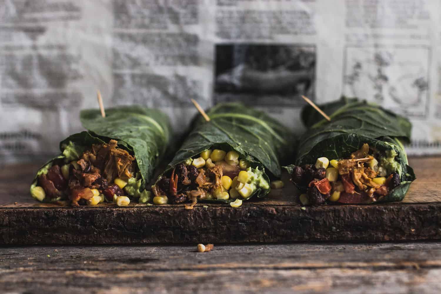 Jackfruit Burrito wrapped in collard leaf lying on a thin wooden cutting board with newspaper as a background