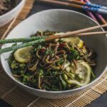 Soba noodle, edamame, sliced lemon in a white bowl with two chopsticks over the bowl