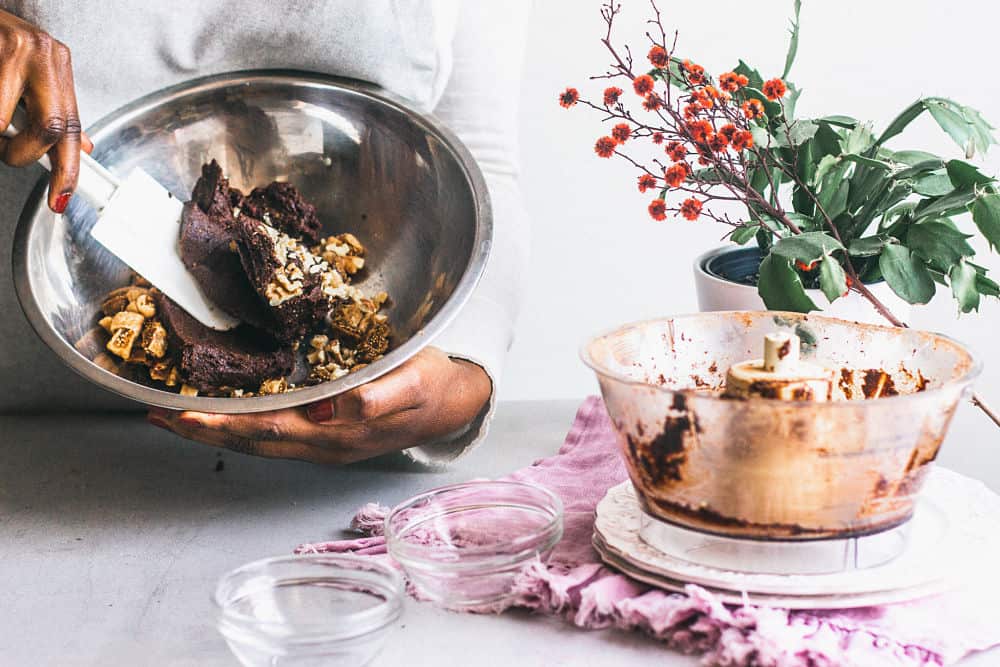 A bowl of a brownie dough being held by a dark-skinned hands