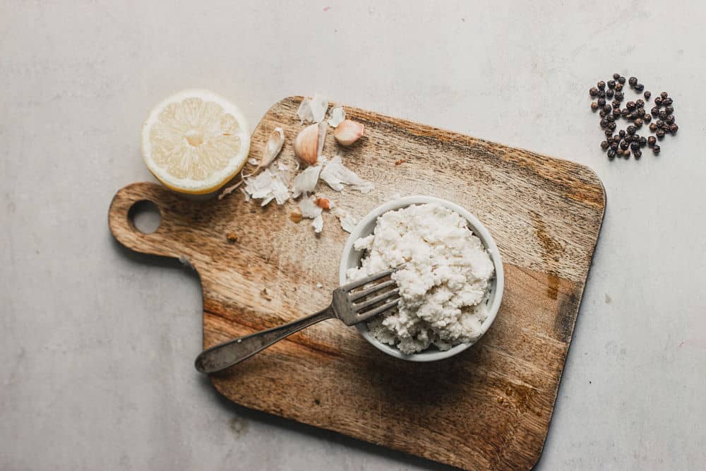 Bird's eye view of a ricotta style cheese in a ramekin on top of a small wooden cutting board