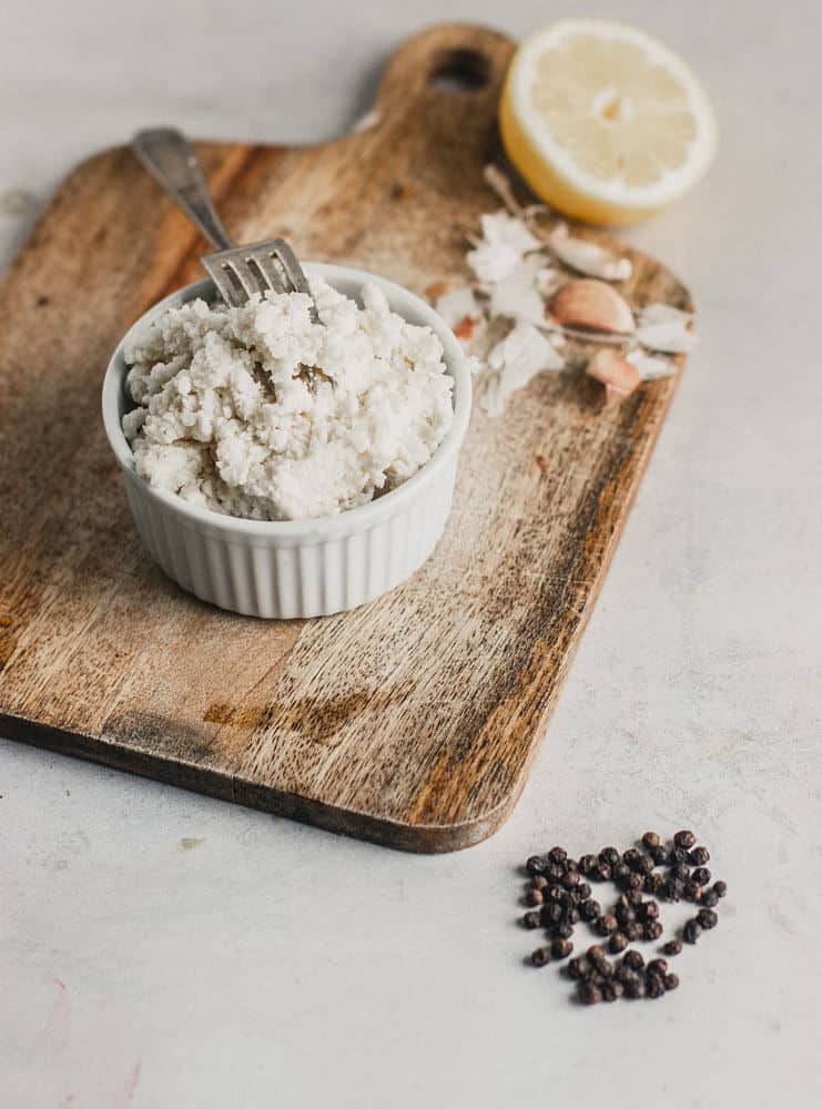 Ricotta style cheese in a ramekin on top of a small wooden cutting board