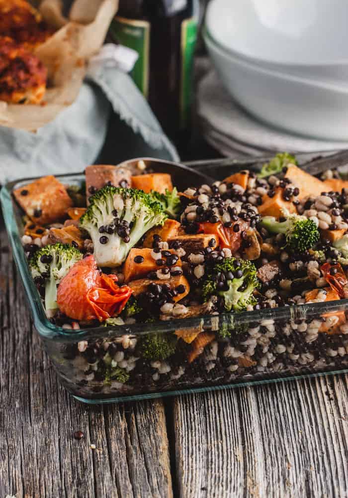 Lentil, pearl barley and sweet potato salad in a baking dish surrounded by stacked plates and bowls