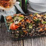 Lentil, barley, and sweet potato salad with broccoli and baby tomatoes in a glass baking dish sitting on a wooden board