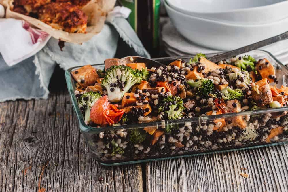 Lentil, pearl barley and sweet potato salad in a baking dish surrounded by stacked plates and bowls