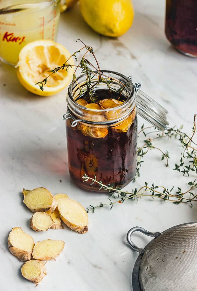 A small jar on maple syrup, thyme sprigs, and slices of ginger