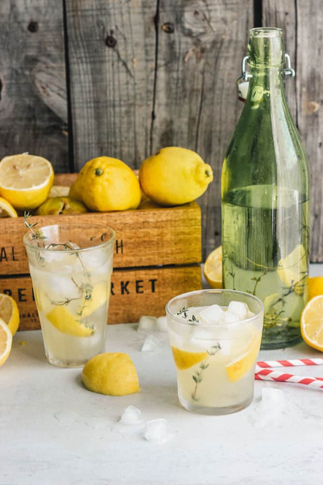 Two glasses of lemonade in front of a small wood container of lemons