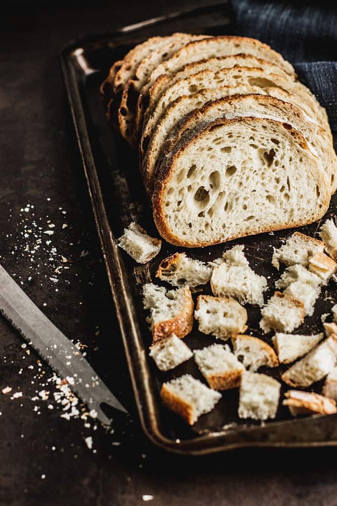 Slices of bread behind cubes of bread in a baking sheet