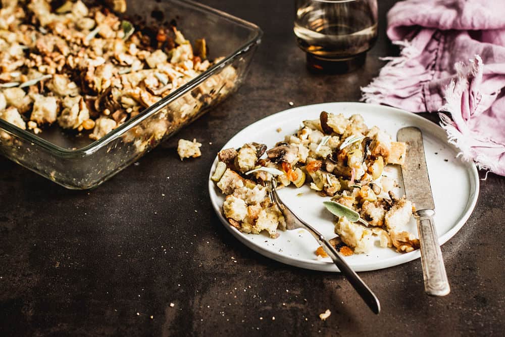 vegan stuffing on white rounded plate with a casserole dish in the background