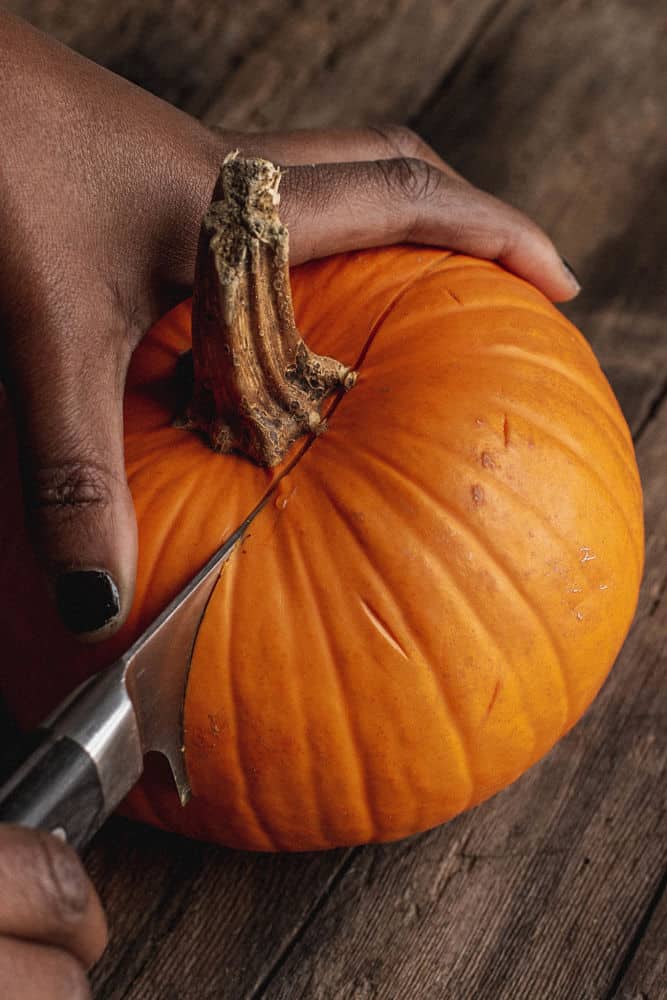 Dark-skinned hand holding and cutting a small pumpkin crosswise