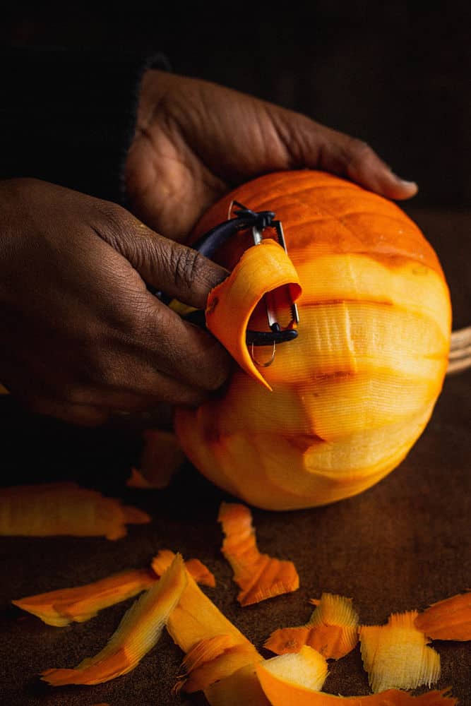 A dark-skinned hand holding and cutting a small pumpkin crosswise