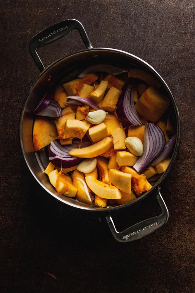 Overhead view of pieces of pumpkin, onion, and garlic in a pot for steaming