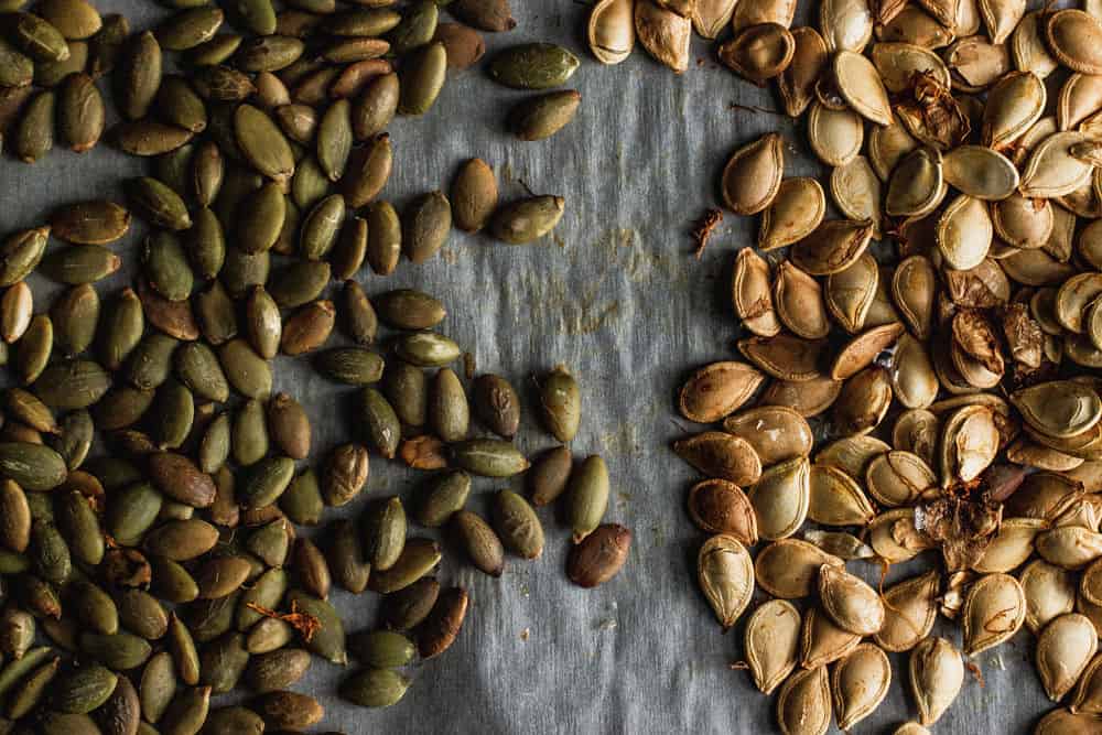 Bird's eye view of roasted green pumpkin seeds on the left next to yellow pumpkin seeds to the right