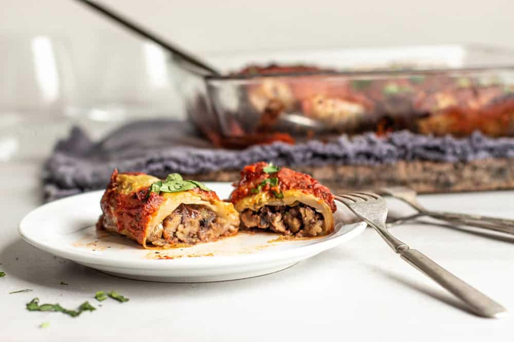 Stuffed cabbage rolls with tomato sauce on top cut into on a white salad plate with a casserole dish in the background