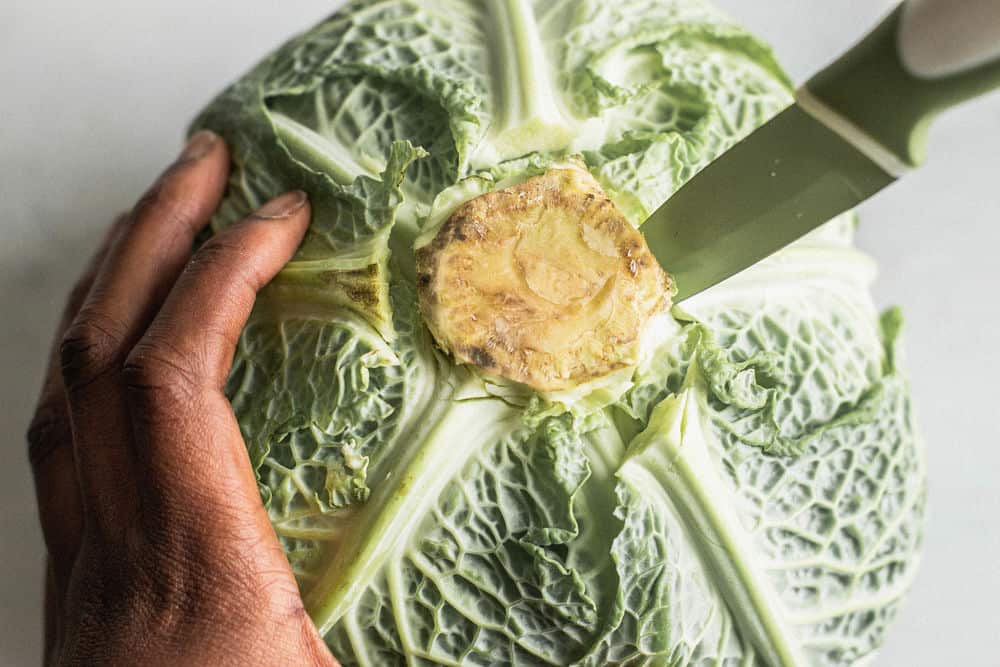 Bird's eye view of a dark-skinned hand holding a cabbage turned upside down with vegetable knife stabbed inside