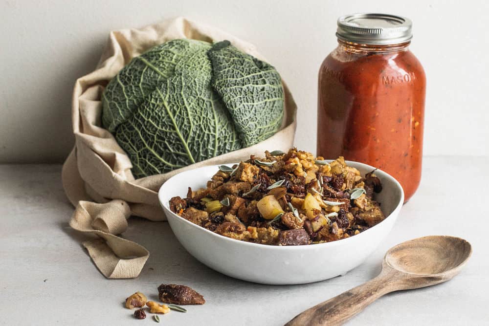 Savoy cabbage in a cloth bag with a white bowl of stuffing and a medium jar of tomato sauce