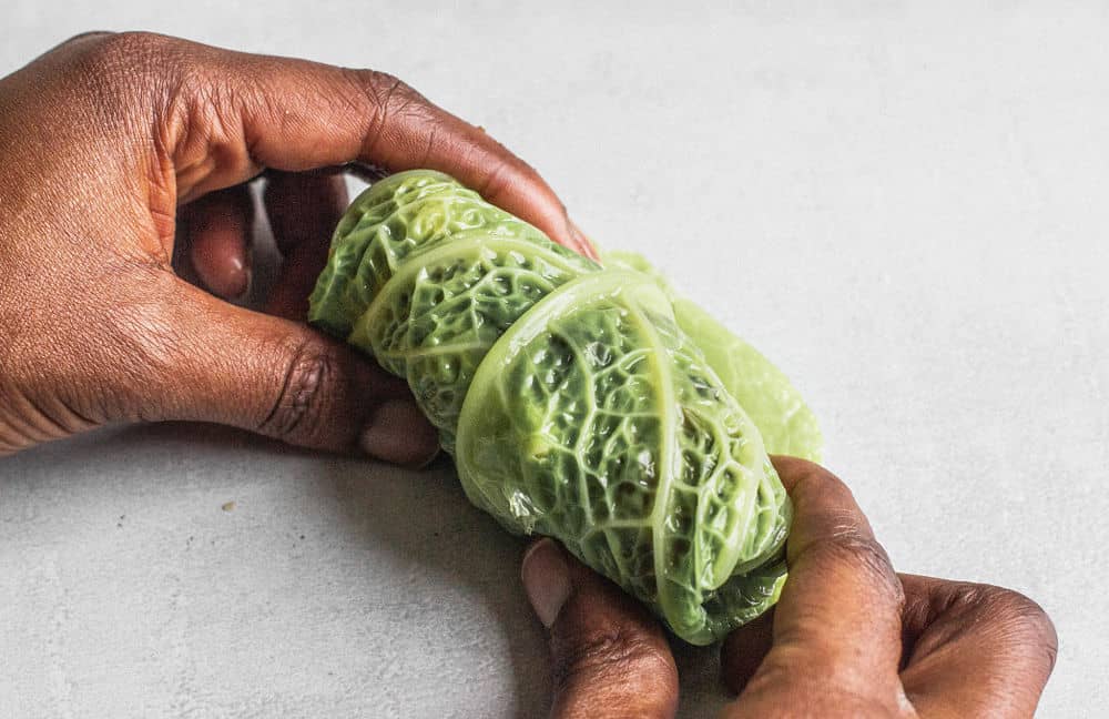 Dark-skinned hands rolling a Savoy cabbage leaf