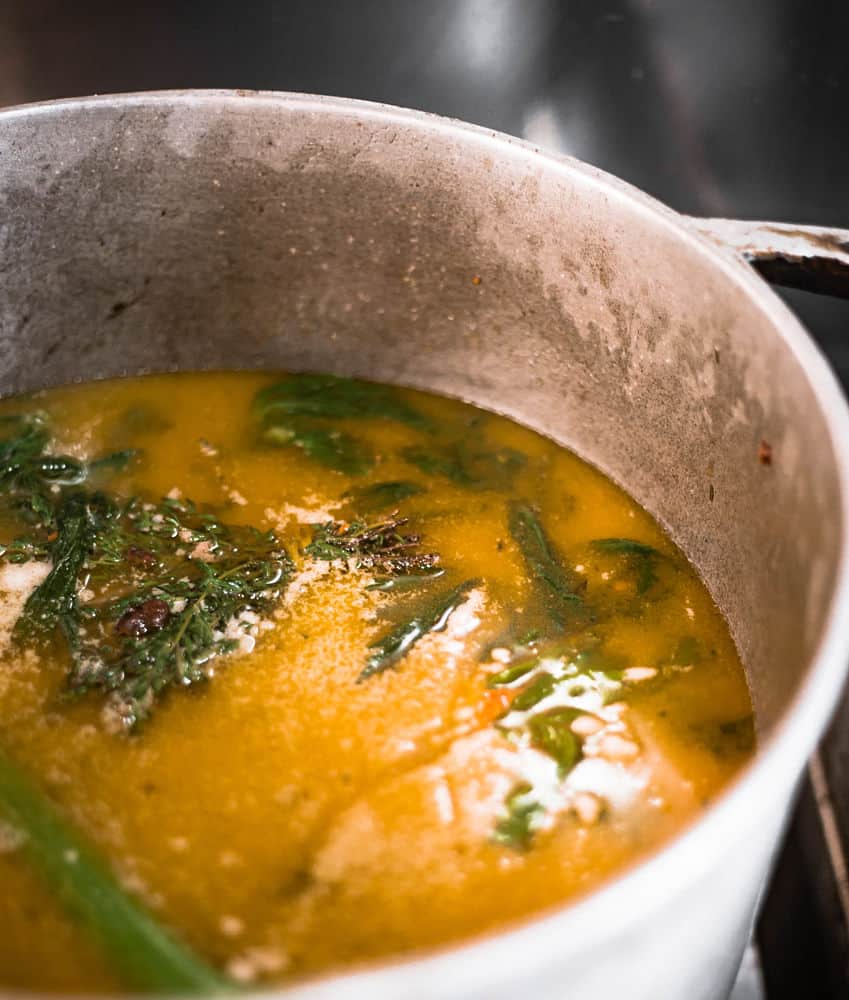 An orange liquid with herbs are simmering in a large pot