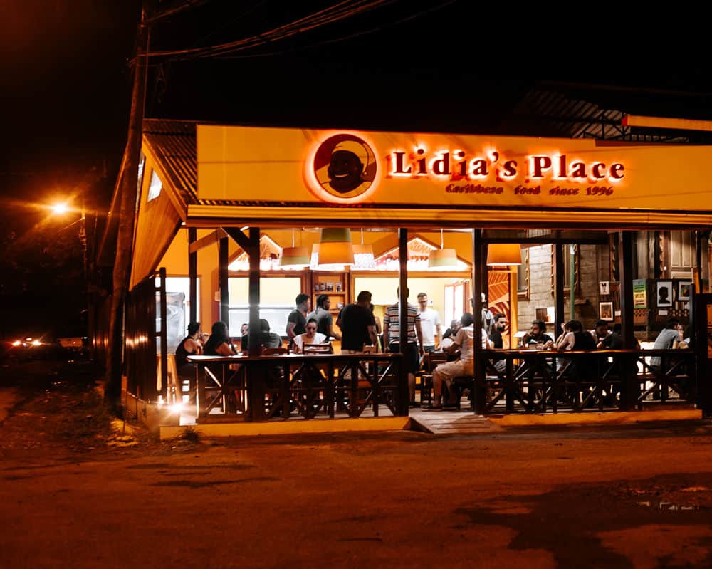 Drawing of an Afro-Caribbean mama with a scarf on her head next to Lidia's Place sign at night in Puerto Viejo