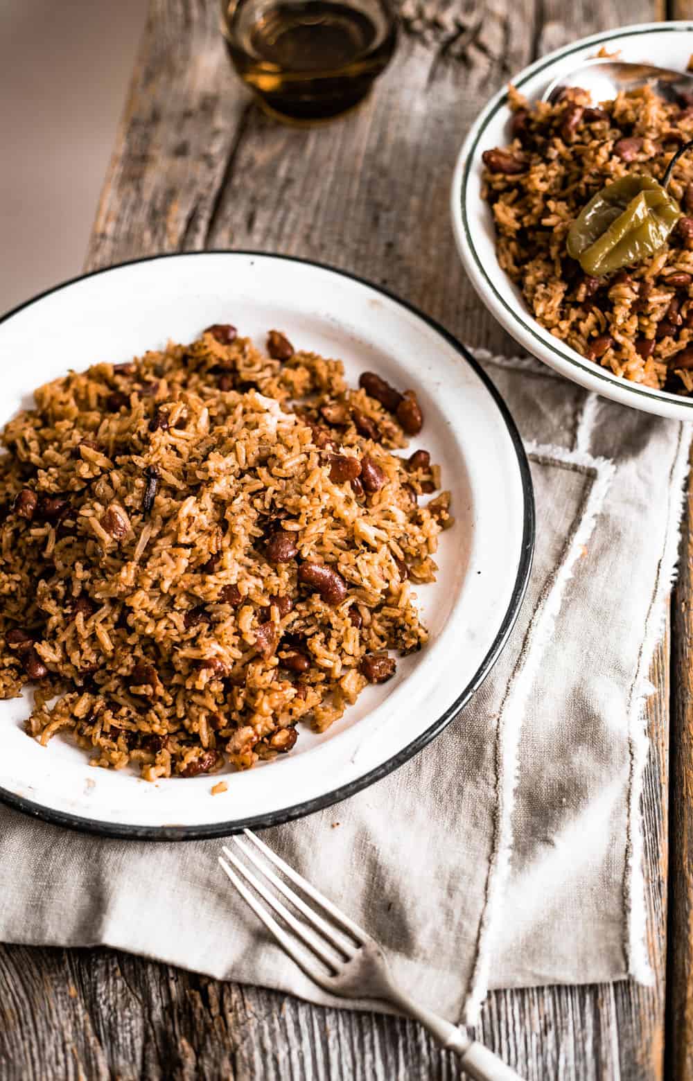 Two plates of Caribbean Rice and Beans on white plates on a wooden board