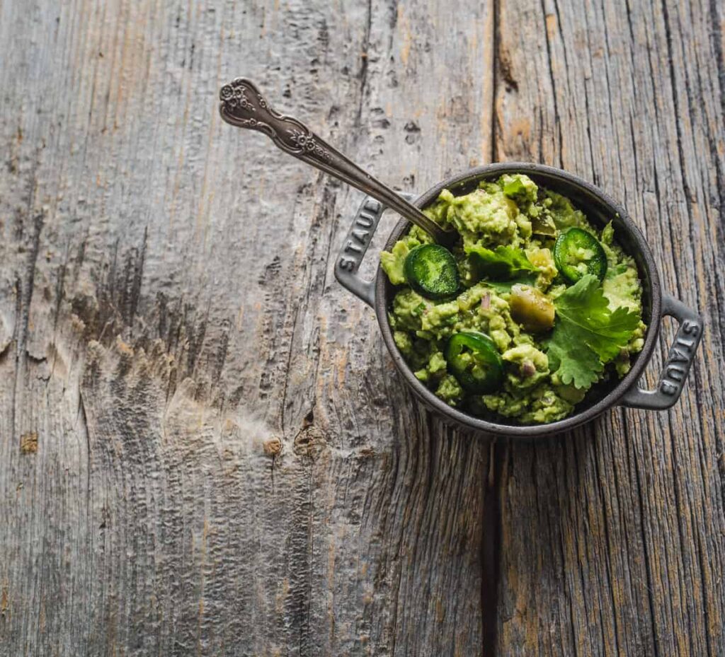 Cumin Guacamole with sliced jalapeno in a small pot on a wooden board