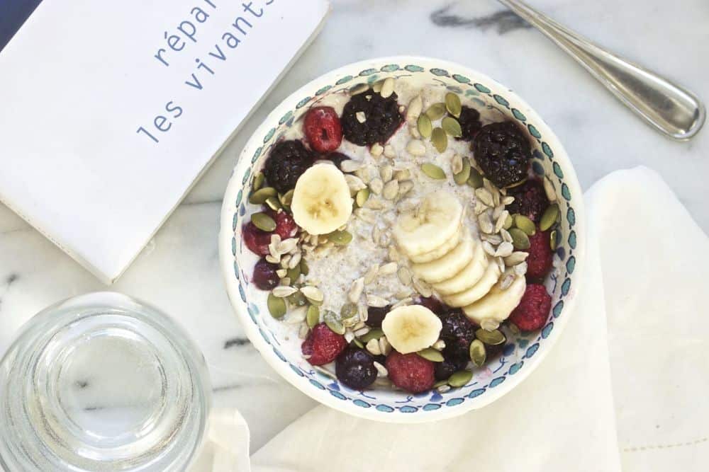 Top view of chia pudding with sliced bananas, berries, pumpkin seeds and sunflower seeds in a colorful bowl