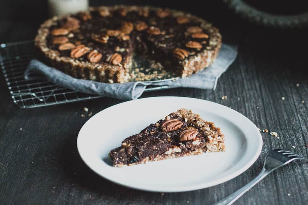 Tranche de tarte aux pacanes dans une petite assiette avec la tarte aux pacanes entière derrière elle