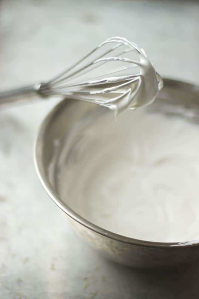 Whipped coconut cream in a bowl with whip leaning on top if it.