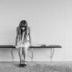 A long-haired girl with her head down sitting on a bench