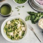 Overhead view of ribbon-shaped pasta with green peas and ricotta, topped in a green sauce