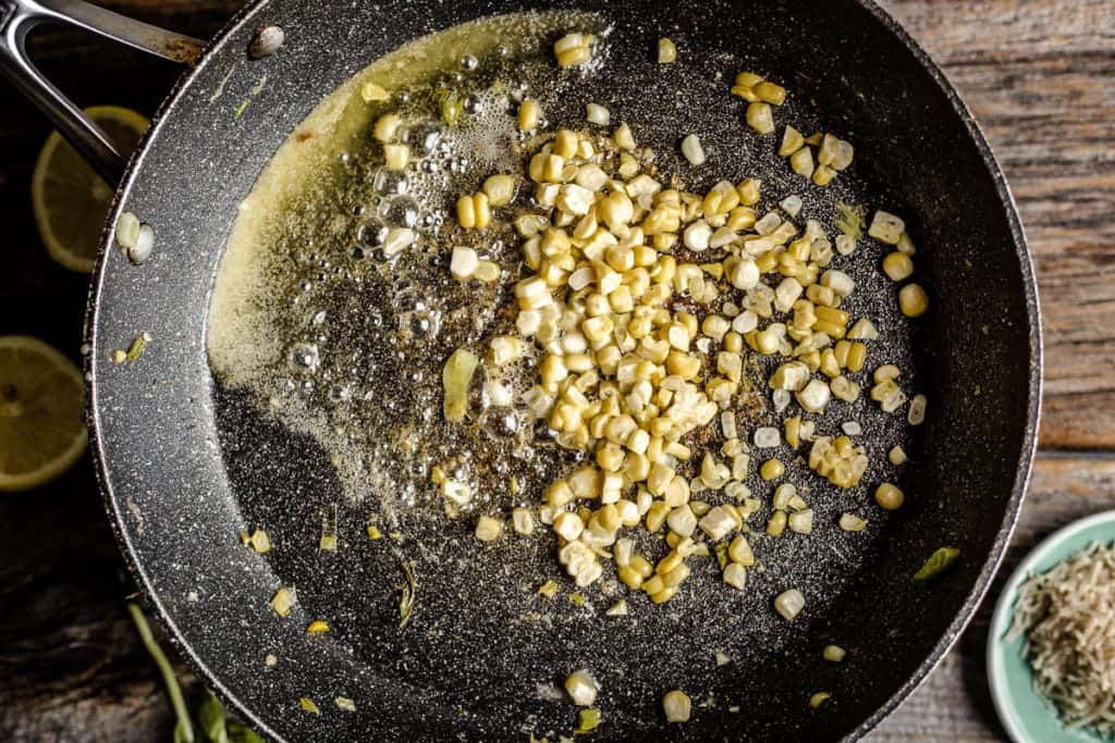 Overhead view of corn kernels sautéing in butter in a skillet