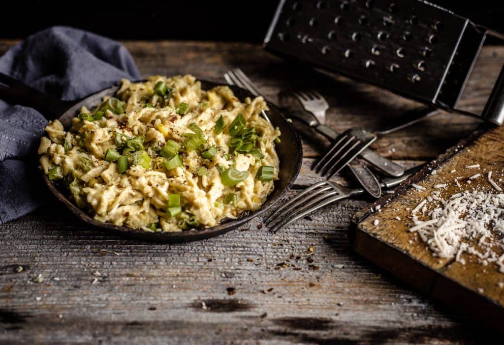 Creamy corn fusilli with green onions and basil in a cast-iron pan on a wooden board and other decorative items