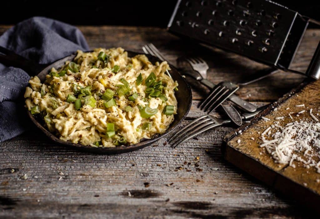 Fusilli au maïs crémeux avec oignons verts et basilic dans une poêle en fonte sur une planche en bois et autres objets décoratifs