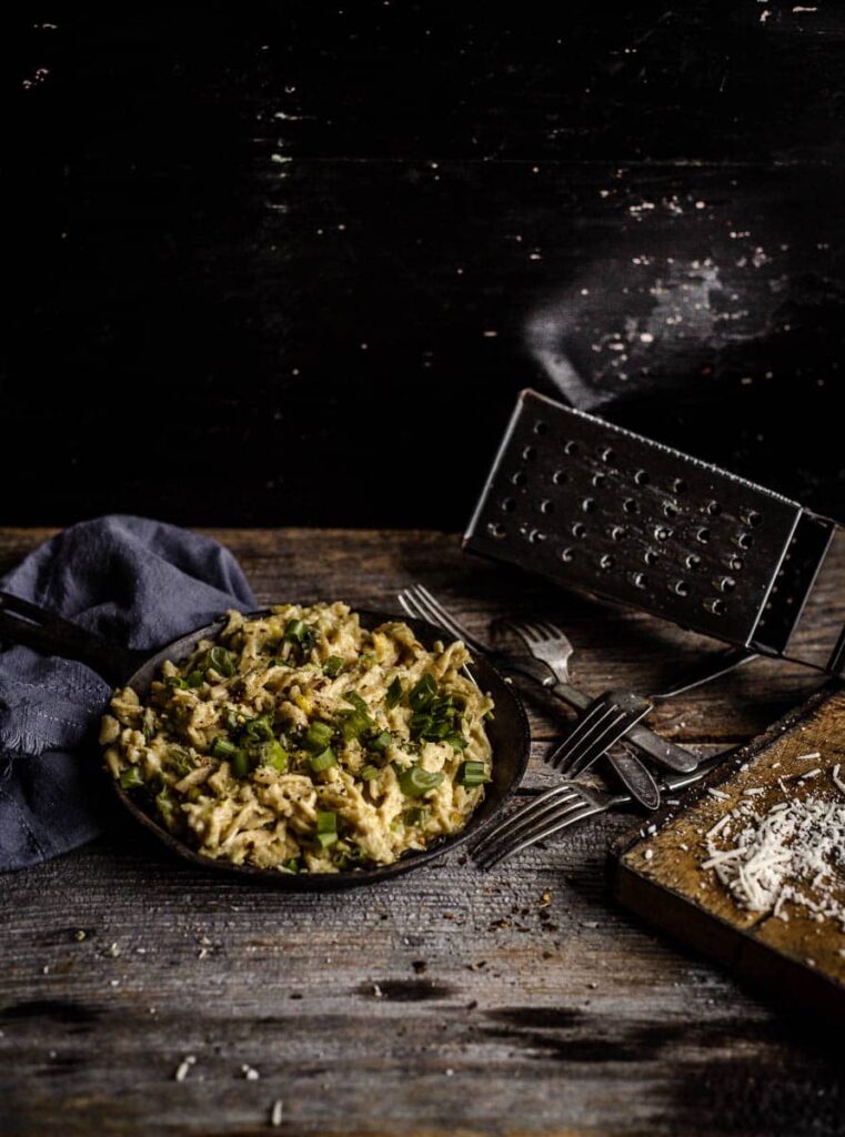 Fusilli au maïs crémeux avec oignons verts et basilic dans une poêle en fonte sur une planche en bois et autres objets décoratifs