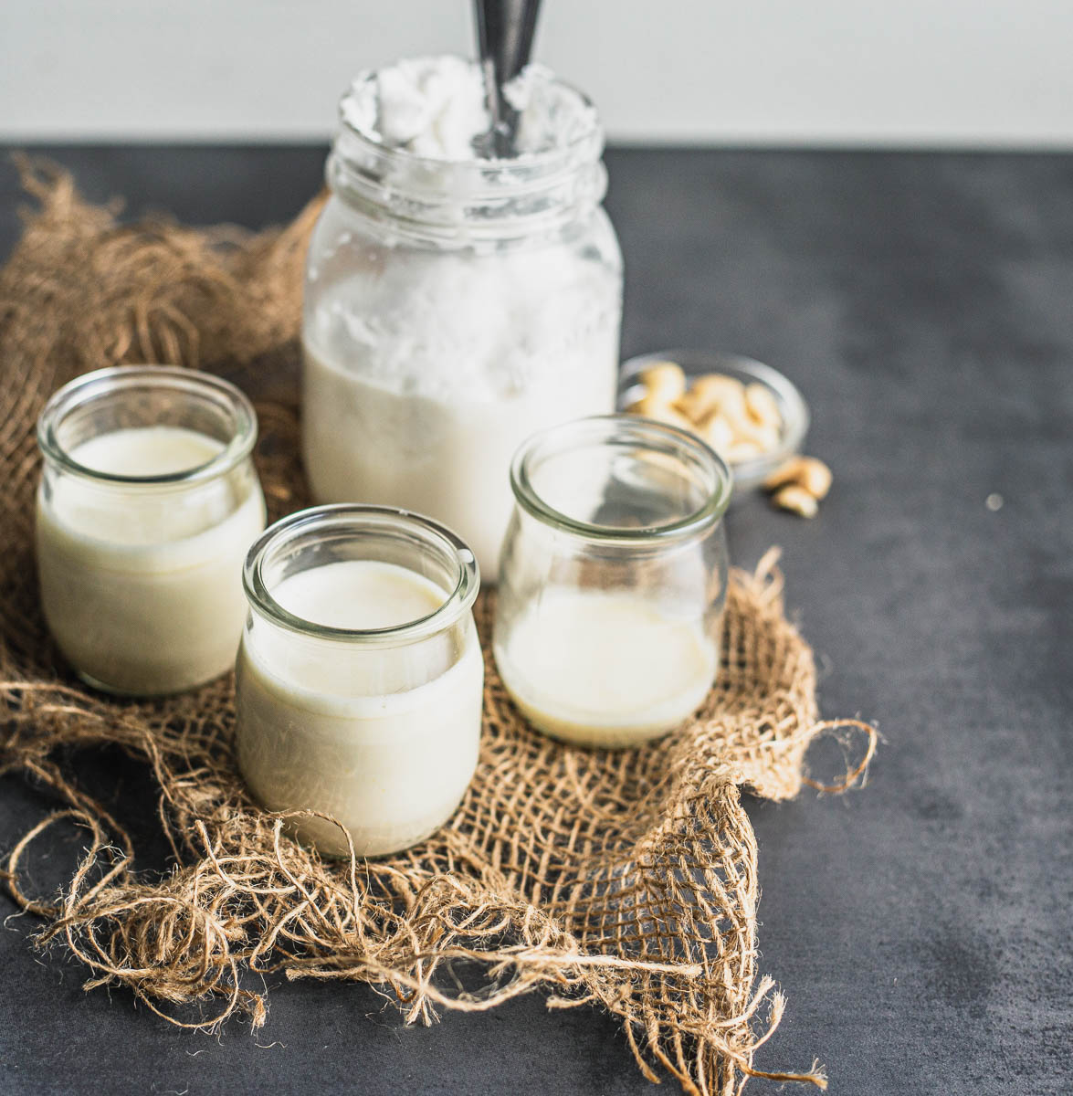 Crème végétale moitié-moité faite maison dans trois petits pots en verre et devant un petit pot Masson de crème de noix de coco, le tout sur un morceau de jute