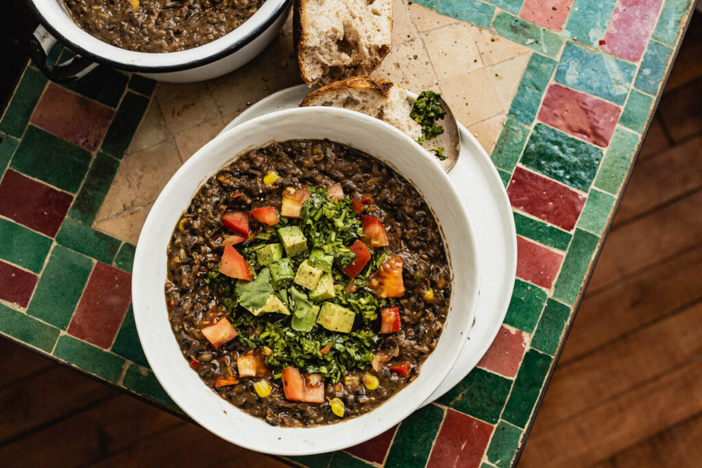 Overhead view of black bean soup speckled with corn and topped with cubed avocado, cubed tomatoes, and cilantro sauce