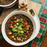 Overhead view of black bean soup speckled with corn and topped with cubed avocado, cubed tomatoes, and cilantro sauce