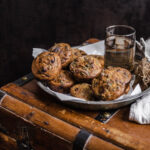 A batch of savory muffins in a metal plate resting on a wooden chest and torn muffin on a narrow cutting board.