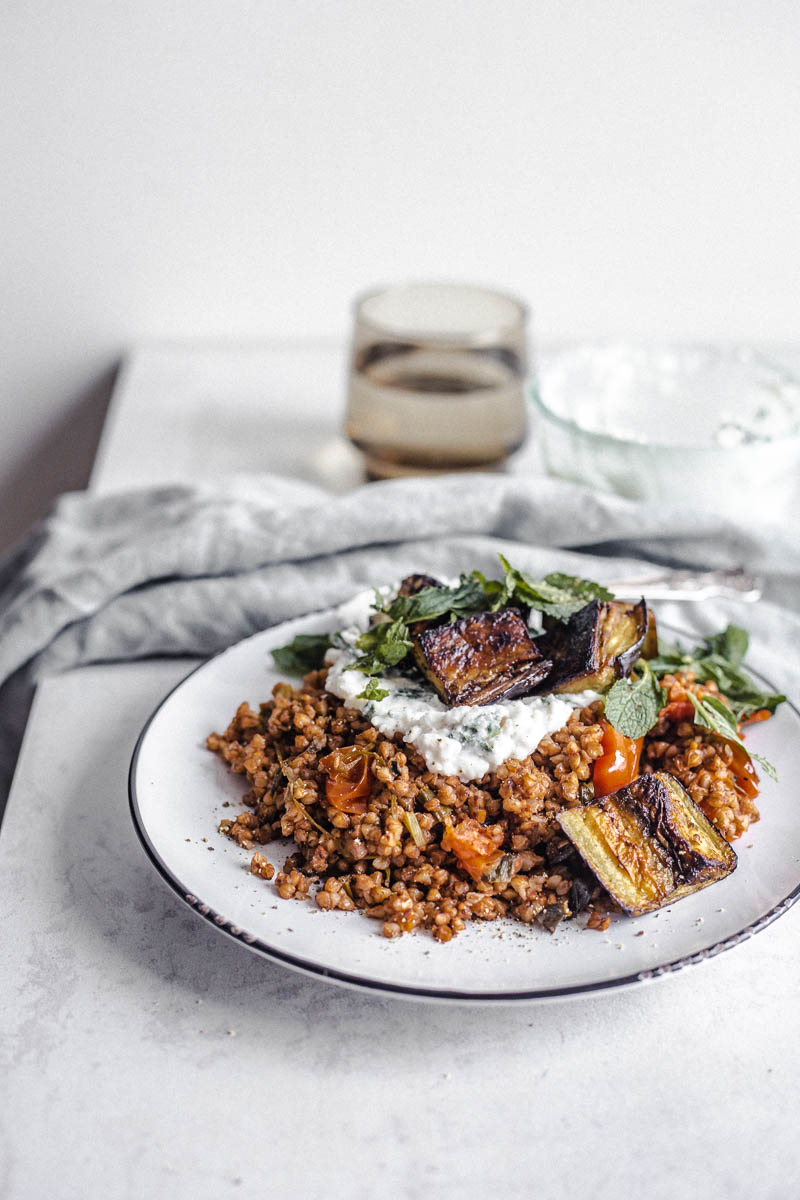 Buckwheat with cherry tomatoes, roasted eggplant, cream cheese style cream, mint on a plate