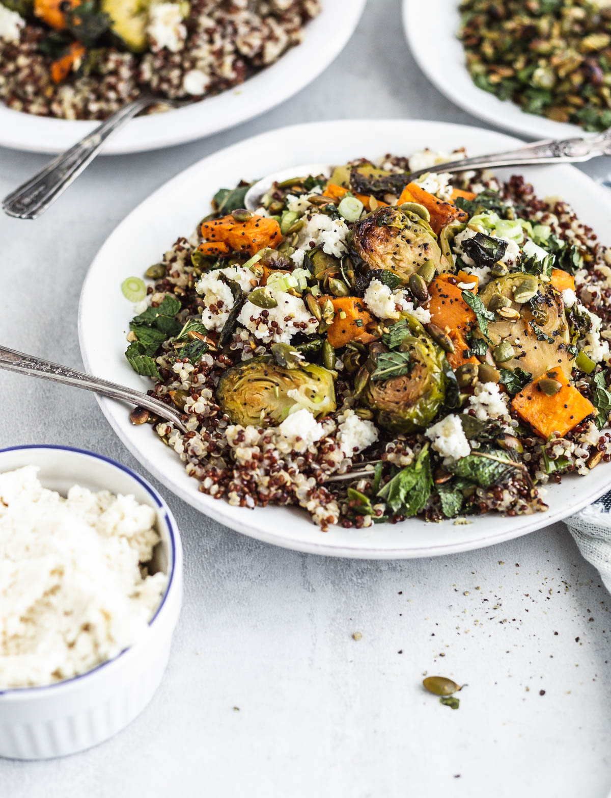 A bowl of quinoa, Brussels sprouts, and sweet potato mixed with vegetable ricotta-style cheese 