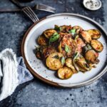 ¾ View of a dish of sliced ​​zucchini, coated in tomato sauce and garnished with torn basil leaf on a round stoneware plate and resting on a metal plate