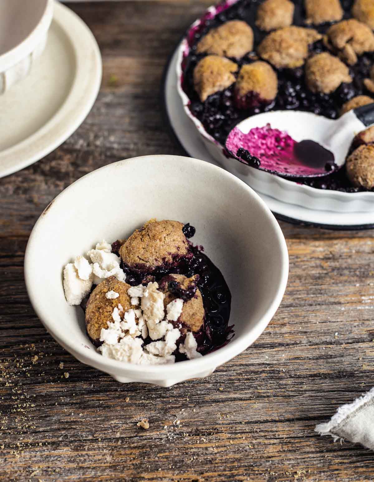 Cobbler aux bleuets garni de crème glacée dans un bol avec un plat de cuisson à l'arrière